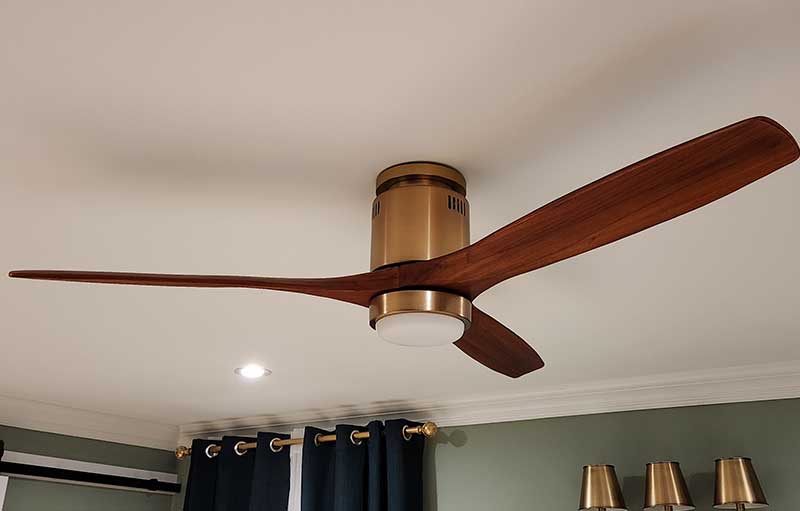 Ceiling fan installation featuring a modern design with wooden blades and a brass finish, complementing residential interiors.