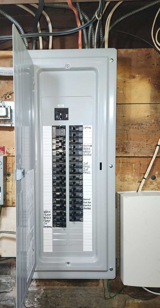Main electrical panel installation with open door, displaying circuit breakers and labeled connections, set against a wooden wall with visible wiring, illustrating electrical service upgrades by Nalset Electrical Services.