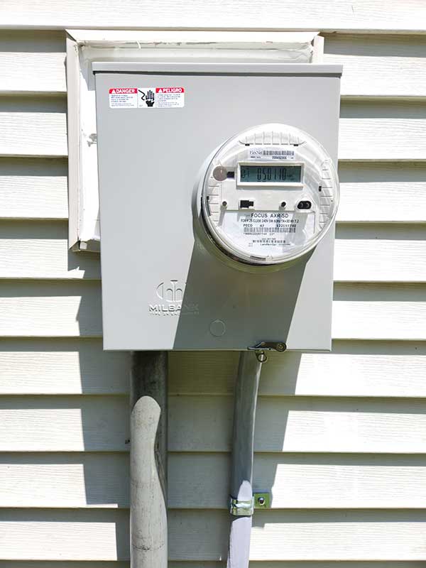 Meter base installation with digital meter, mounted on exterior wall, featuring warning labels and conduit connections, relevant to Nalset Electrical Services' offerings.