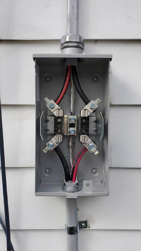Meter base installation showing electrical connections with red and black wires, featuring a gray metal enclosure mounted on a wall.