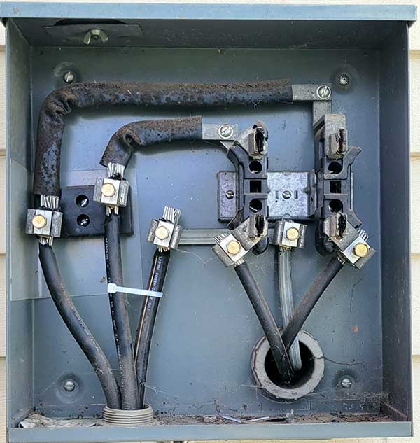 Electrical meter base with exposed wires and connections, illustrating unsafe electrical conditions relevant to electrical safety inspections and emergency repairs.