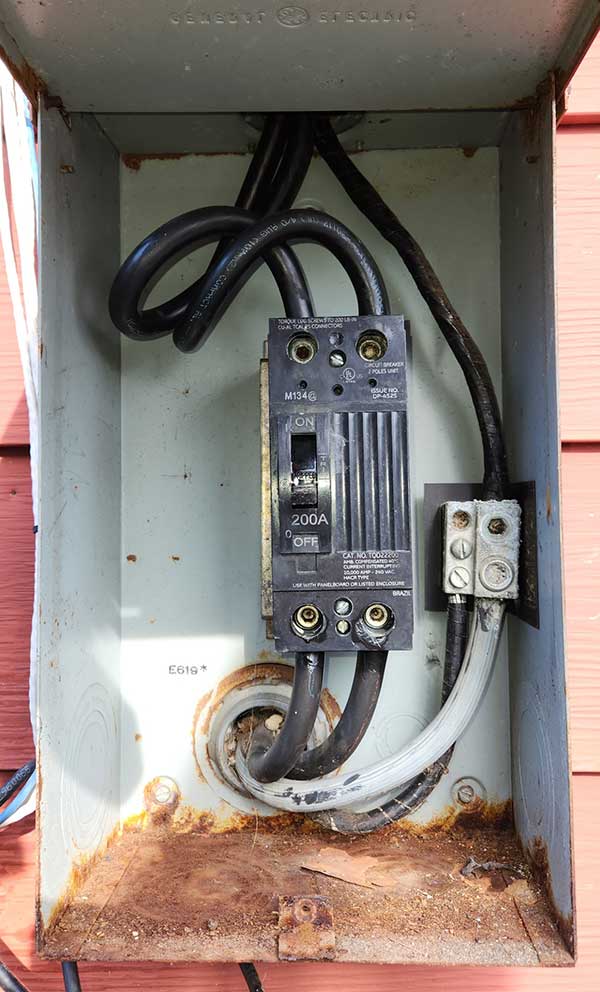 Electrical meter base with visible wiring, circuit breaker labeled 200A, and signs of rust, highlighting unsafe electrical conditions relevant to electrical safety inspections.