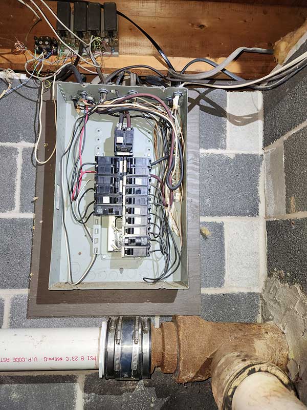 Electrical panel with exposed wiring and circuit breakers, highlighting unsafe electrical conditions in a basement setting, relevant to electrical safety services by Nalset Electrical Services.